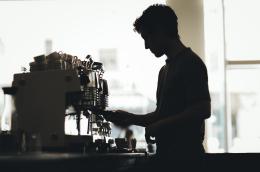 A silhouette profile of a barista working behind an espresso machine.