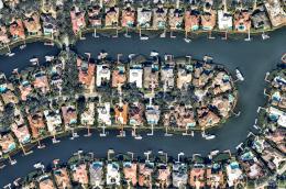An aerial shot of what I swear is my big sister's neighborhood in South Florida, featuring large homes with pools and canals with docks and large boats.