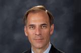 A photo of Mark Zandi. Slight smile, suit, brown hair.