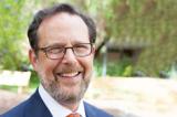 A photo of Jim Millstein outside. Dark hair, big smile, suit and tie, glasses.